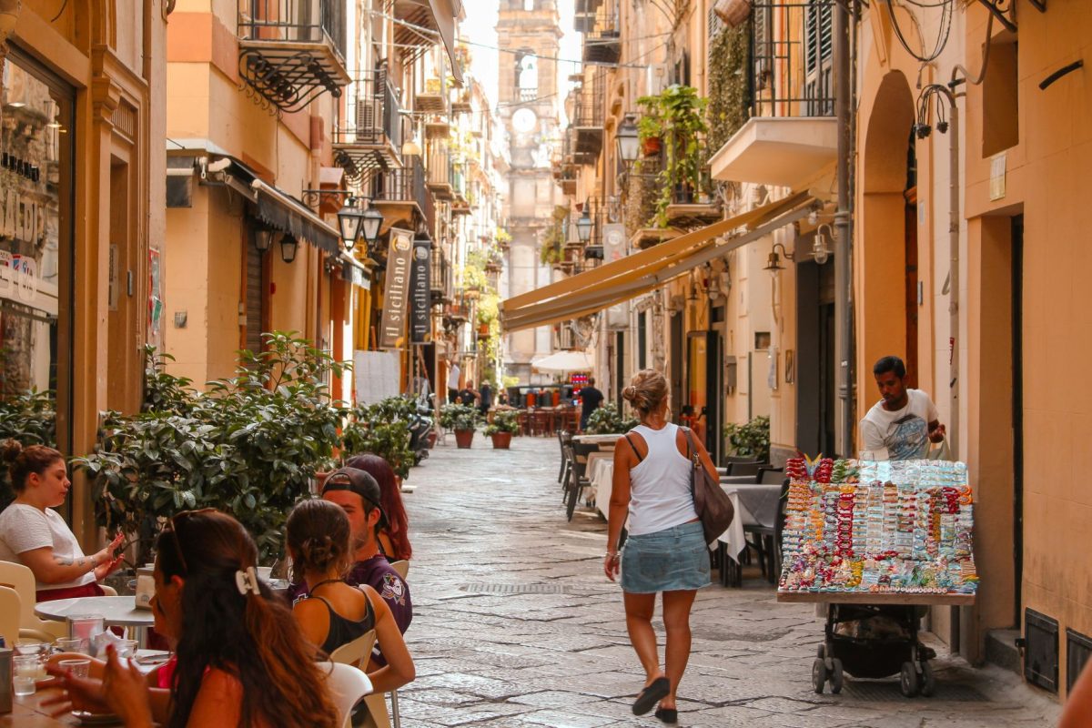 Narrow cobblestone street in a Sicilian town with terracotta buildings and locals