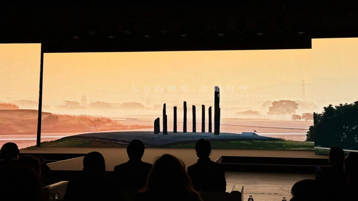Silhouettes of visitors viewing an illuminated modern sculpture against a golden sunset sky
