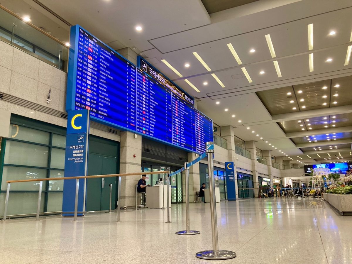 Empty airport terminal with blue departure boards and minimal travelers during travel restrictions