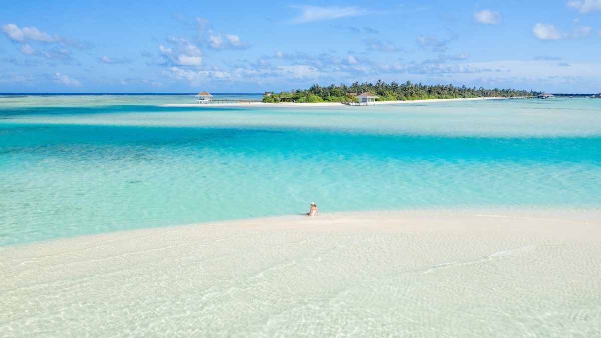 Pristine turquoise lagoon with white sand beach and palm-fringed island under blue sky