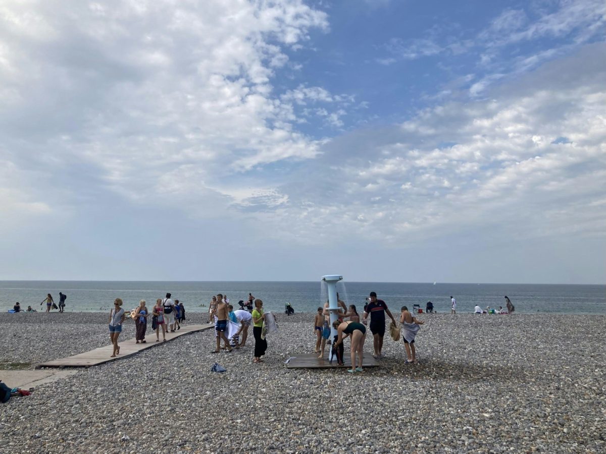 Beachgoers gathering on a pebble beach under a partly cloudy sky