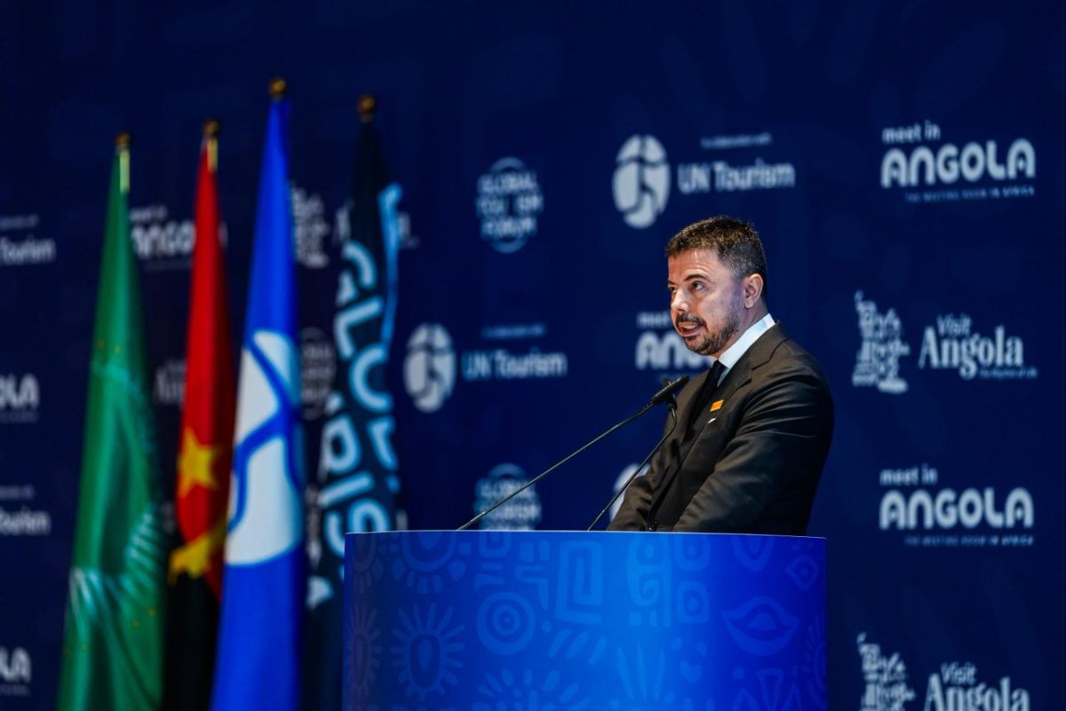 Speaker at podium with national flags and tourism logos in background.
