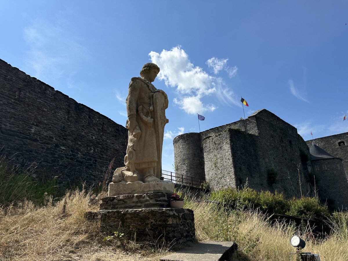 Stone statue overlooking Bouillon Castle ruins with Ardennes landscape