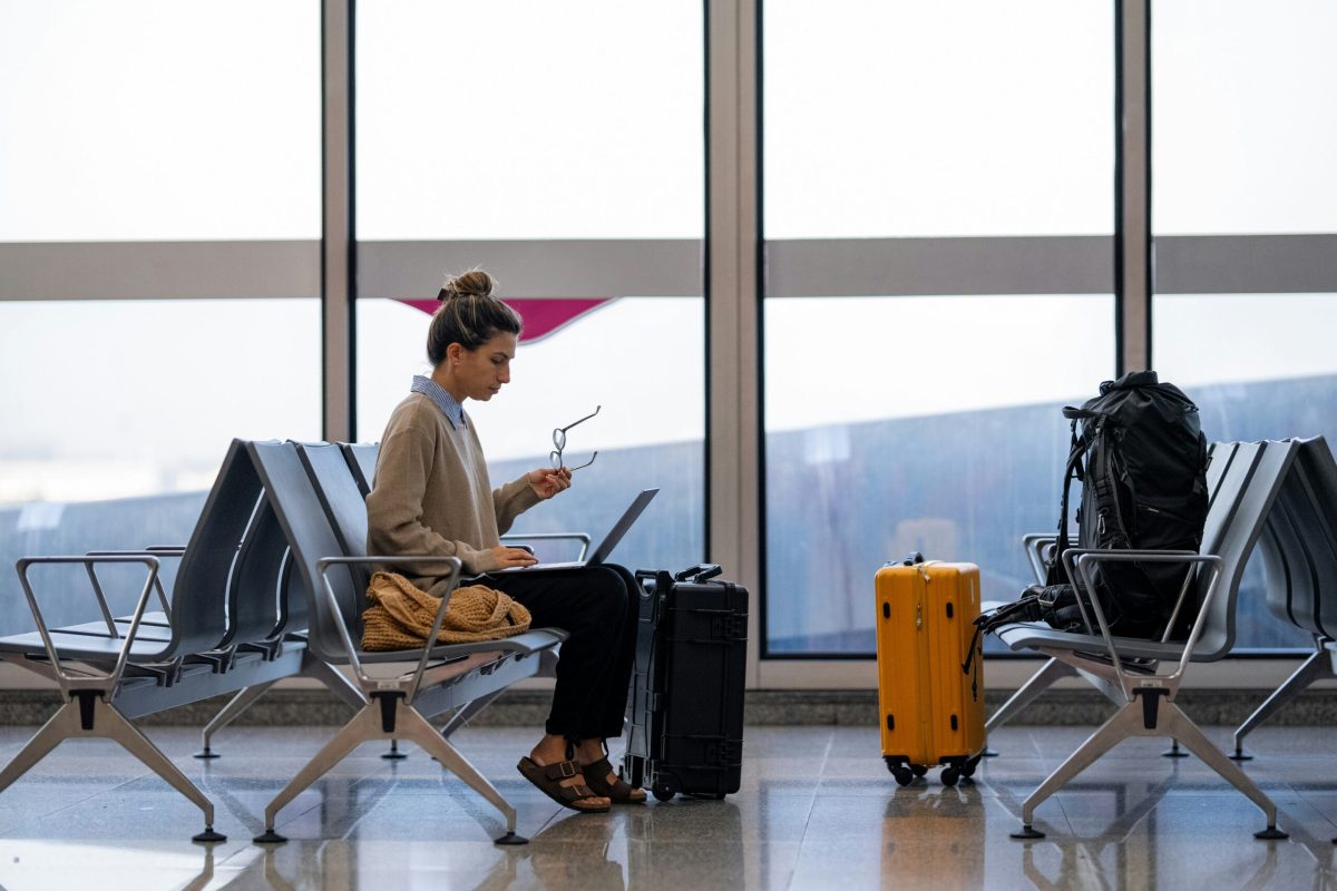 Traveler in casual clothing working on laptop at airport gate near windows