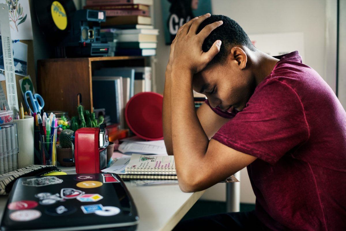 Teenage boy at desk with head in hand, appearing stressed or anxious