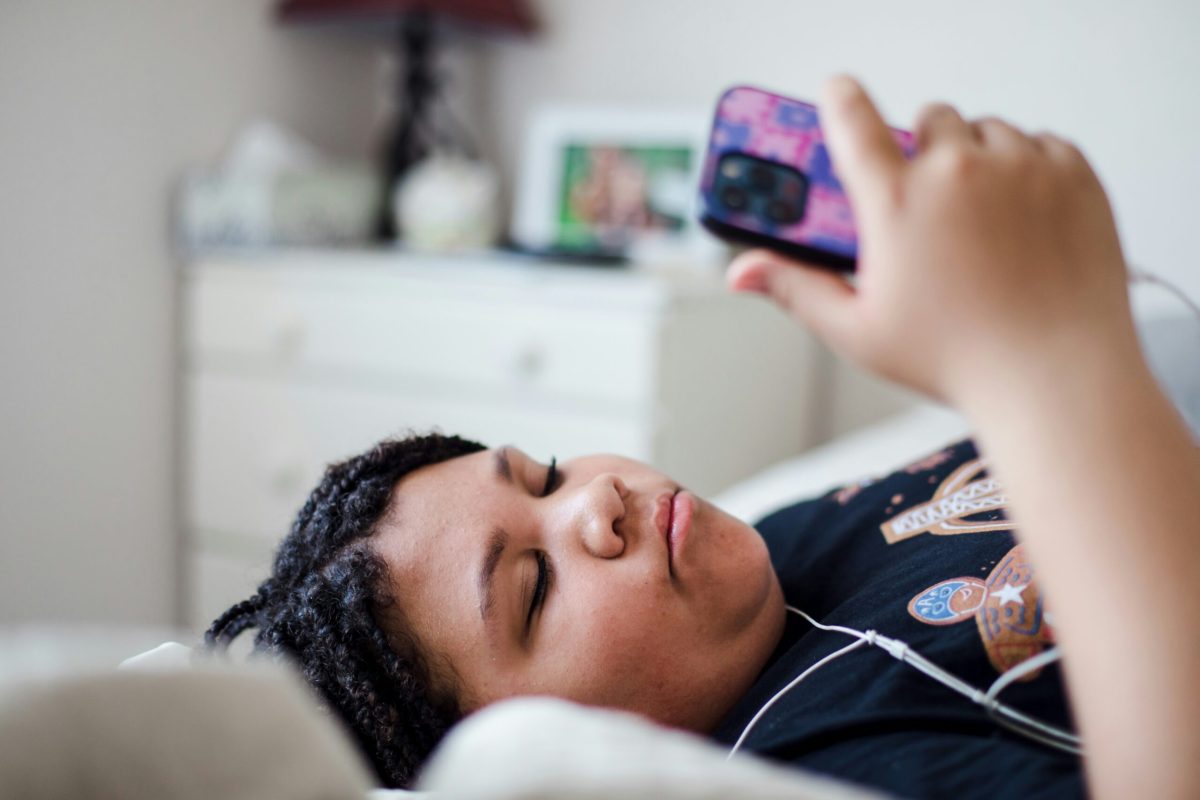 Teenager lying in bed using smartphone with earbuds