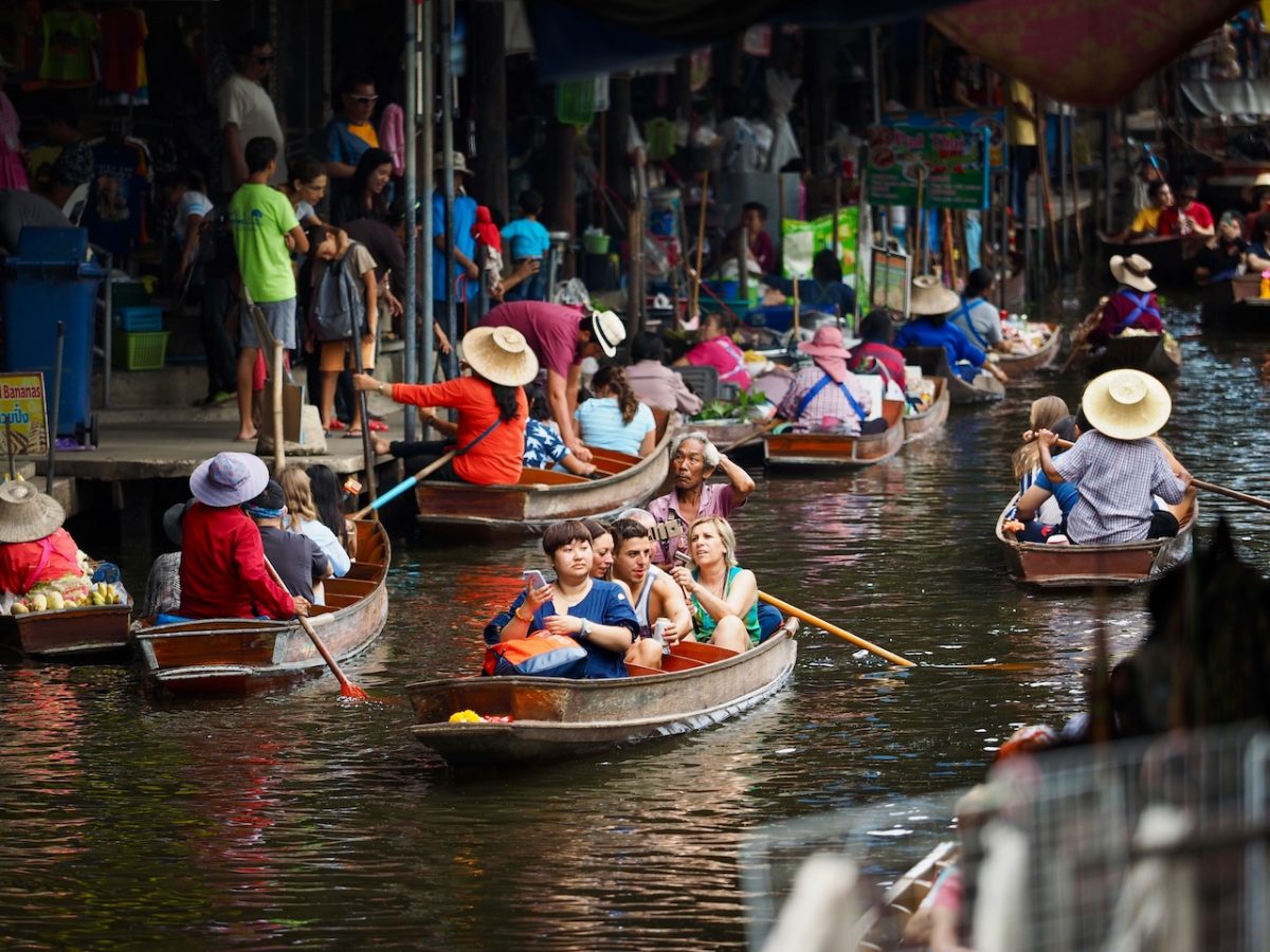 Tourists in traditional wooden boats on a flooded canal market in Thailand wearing hats and life jackets