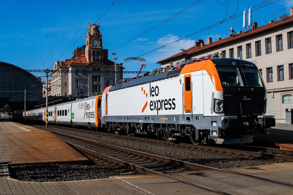 Orange and white RegioExpress train at a European station platform with historic buildings