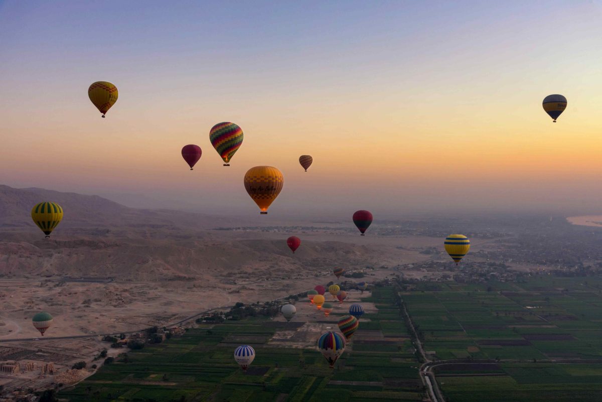 Hot air balloons ascend over a desert landscape at sunrise.