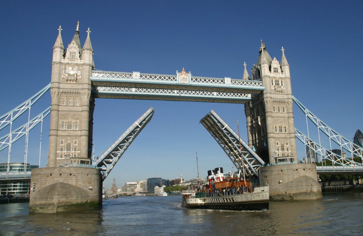 Historic paddle steamer passes under Tower Bridge with the bridge raised.