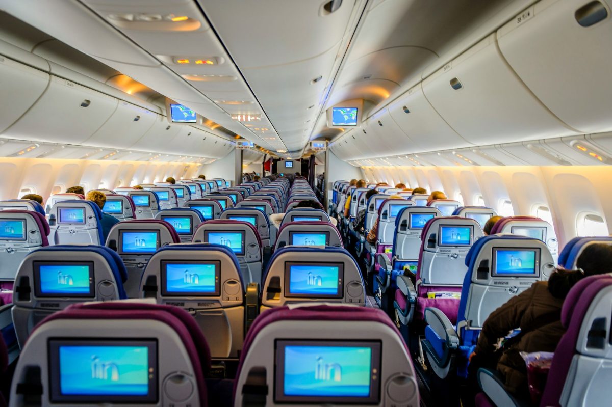 Aircraft cabin interior with rows of blue seats and illuminated seatback screens showing the airline logo