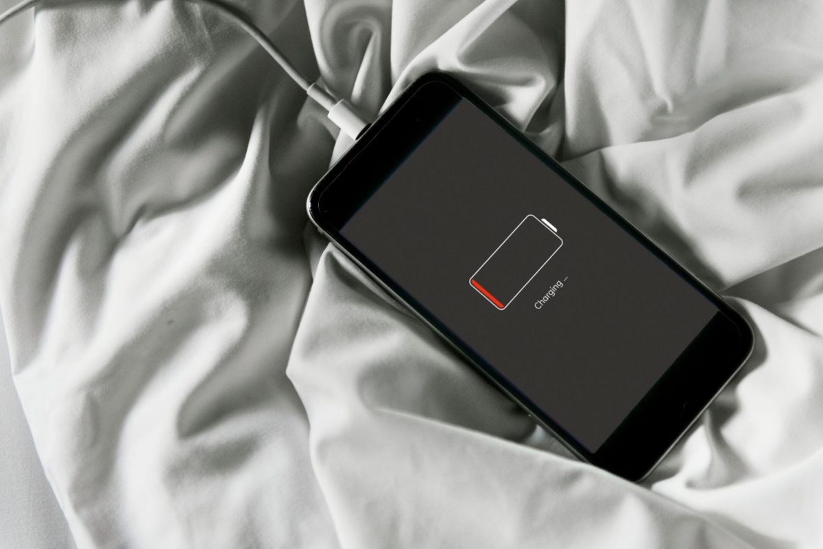 Smartphone with low battery warning displayed on white bedding