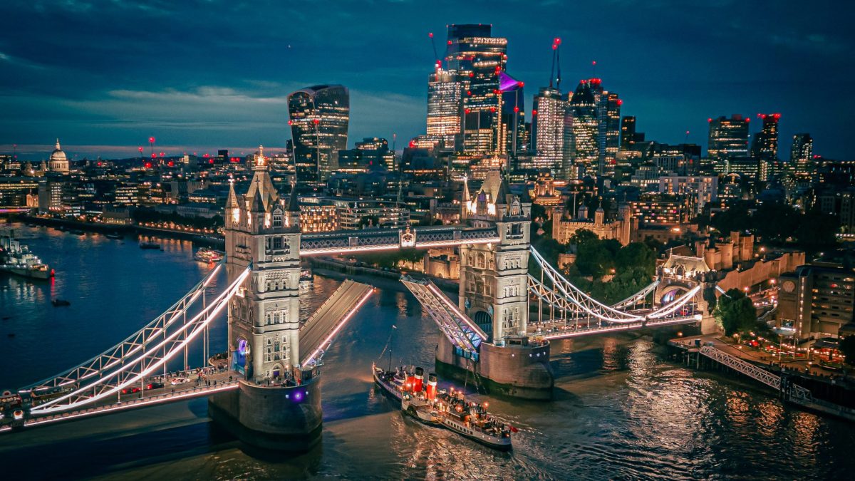 The Waverley paddle steamer cruises past Tower Bridge at dusk, London skyline in background.