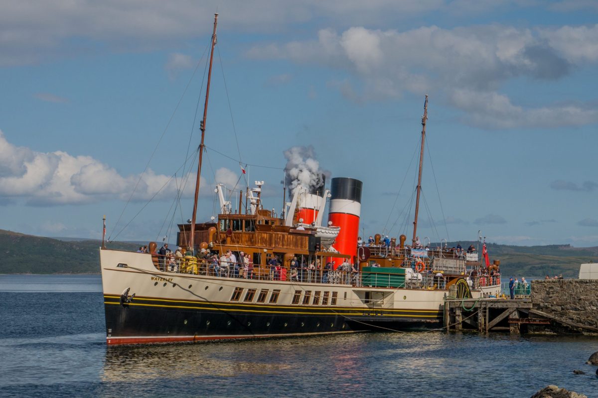The Waverley paddle steamer sailing on a calm sea, with a backdrop of green hills.