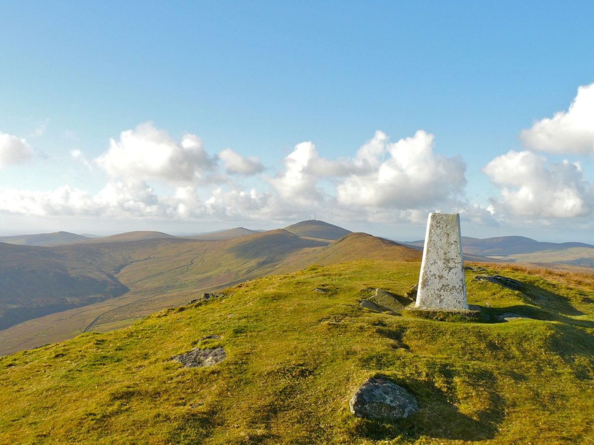 White stone cairn on green hillside with mountains and blue sky in background