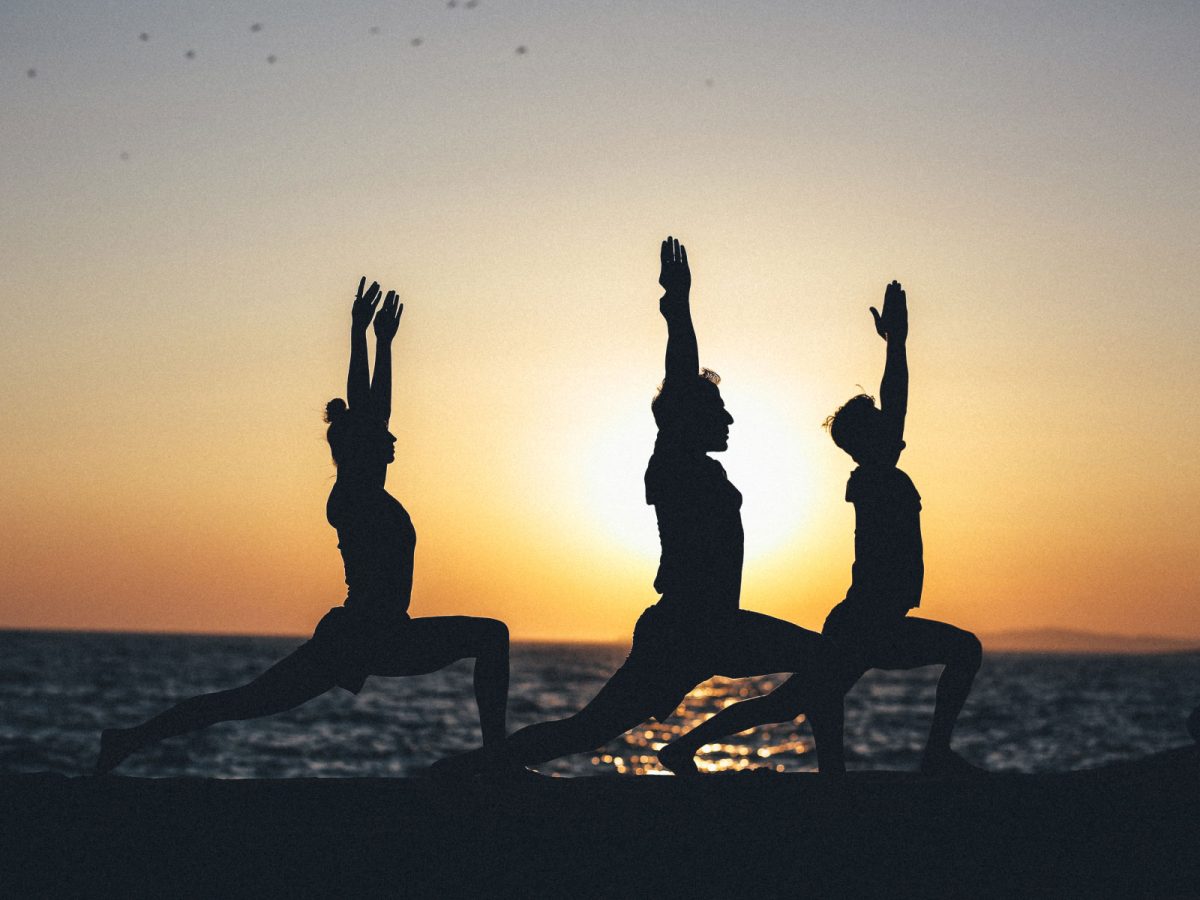 Three people in yoga poses silhouetted against sunset over ocean
