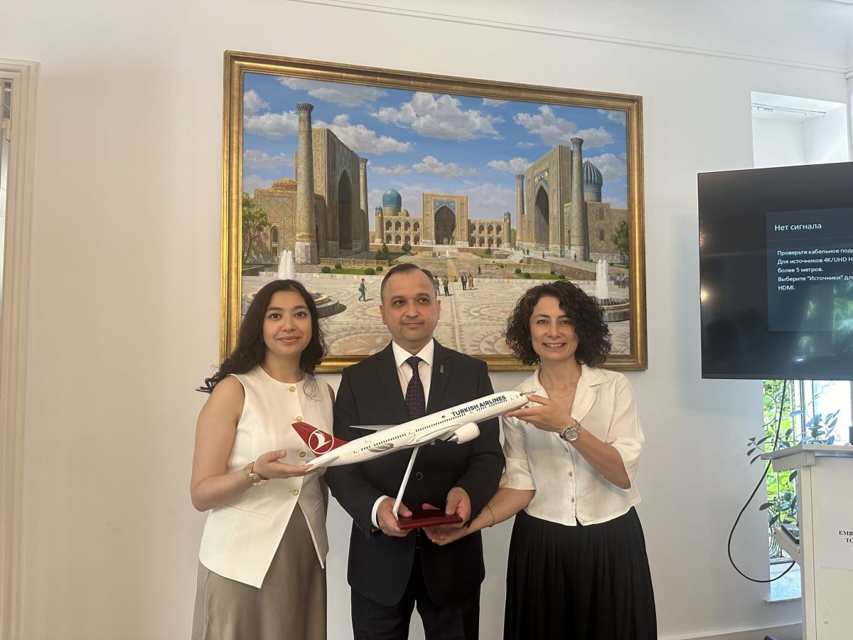 Three tourism officials holding a rolled document in front of a cityscape painting