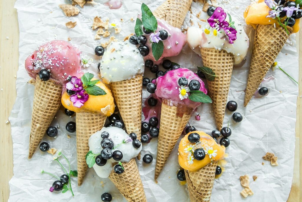 Colorful ice cream cones with fresh berries and flowers on marble surface
