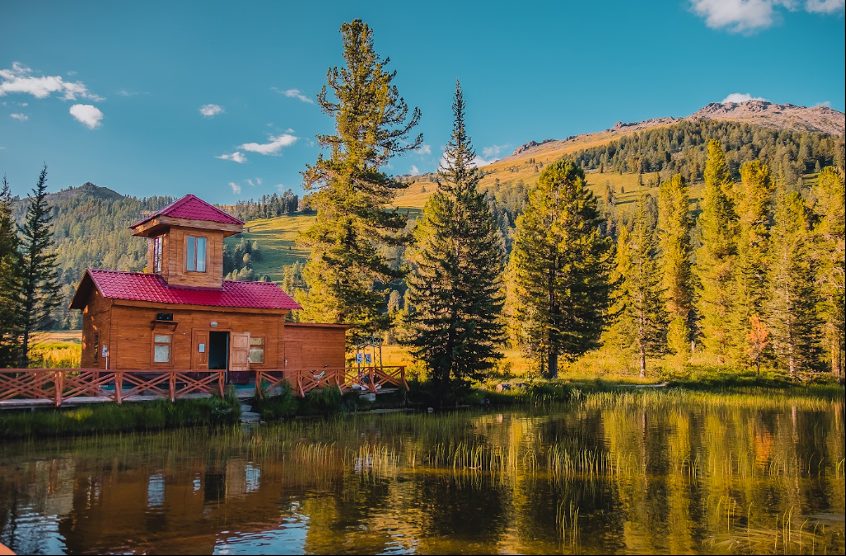 Traditional Kazakh wooden house reflected in a tranquil mountain lake.