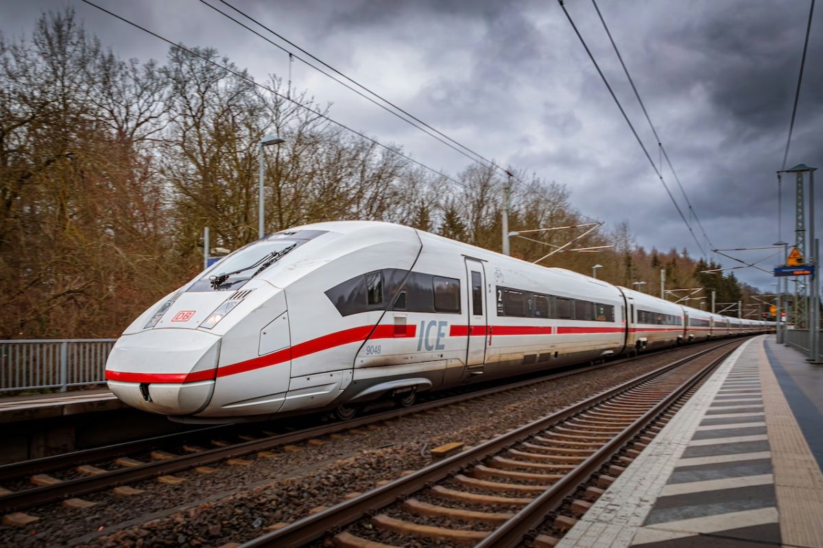 White and red high-speed train at a platform with bare trees and power lines in background