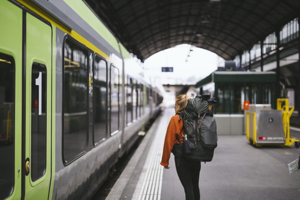 Traveler with backpack boarding a green train at a European railway station