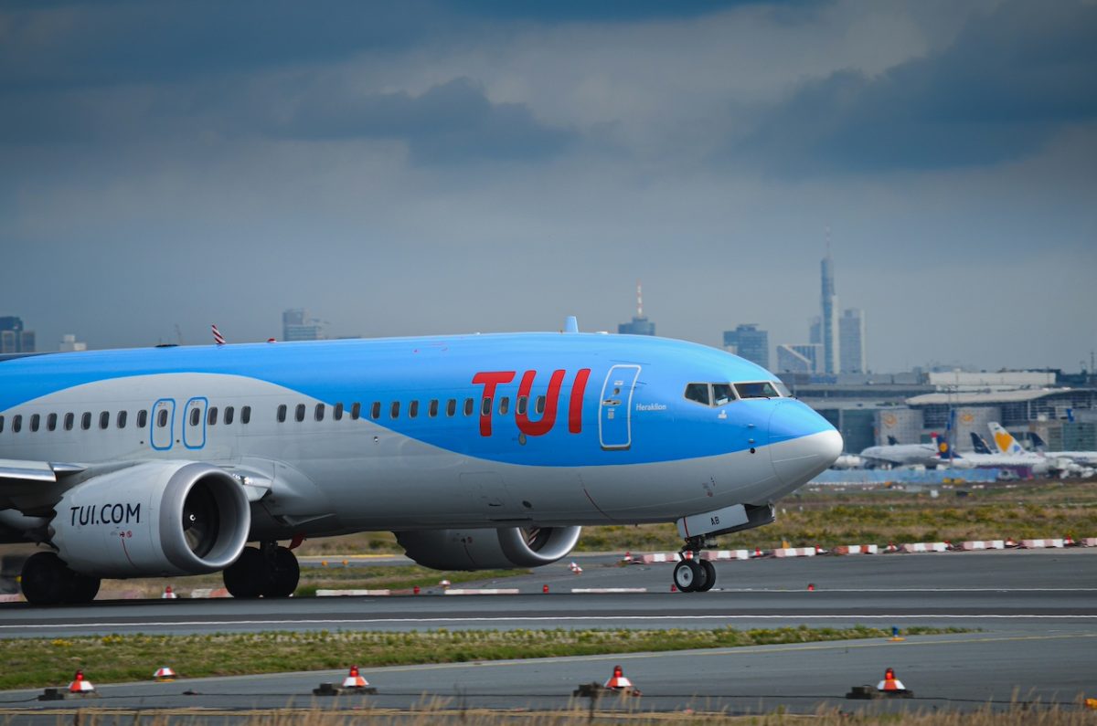 Blue TUI aircraft taxiing on airport runway with city skyline in background