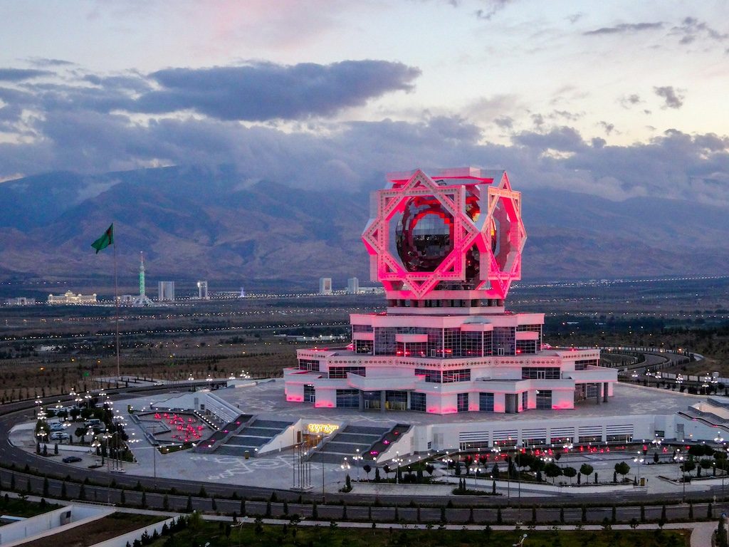 Pink monument with giant rotating sphere overlooking Ashgabat valley at dusk