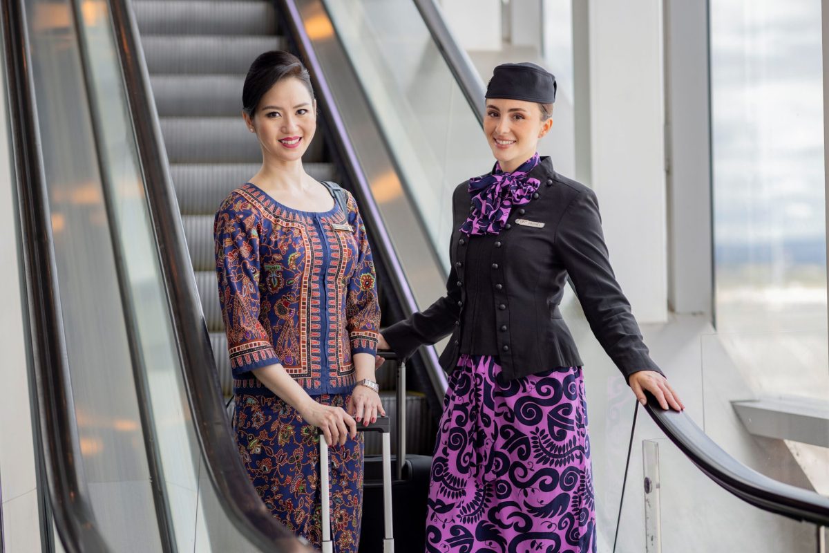 Two airline crew members in traditional purple and black uniforms on an escalator