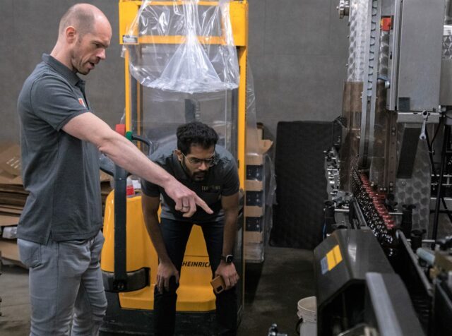 Two brewers examining beer in a wooden barrel at a craft brewery facility
