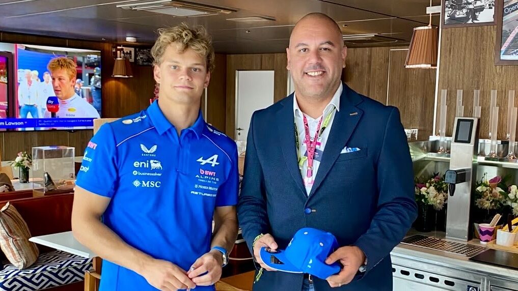 Two men in business casual attire holding blue caps in a modern interior space