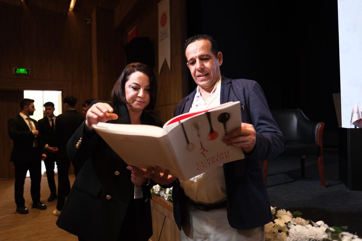 Two people examining a large cookbook or culinary publication together