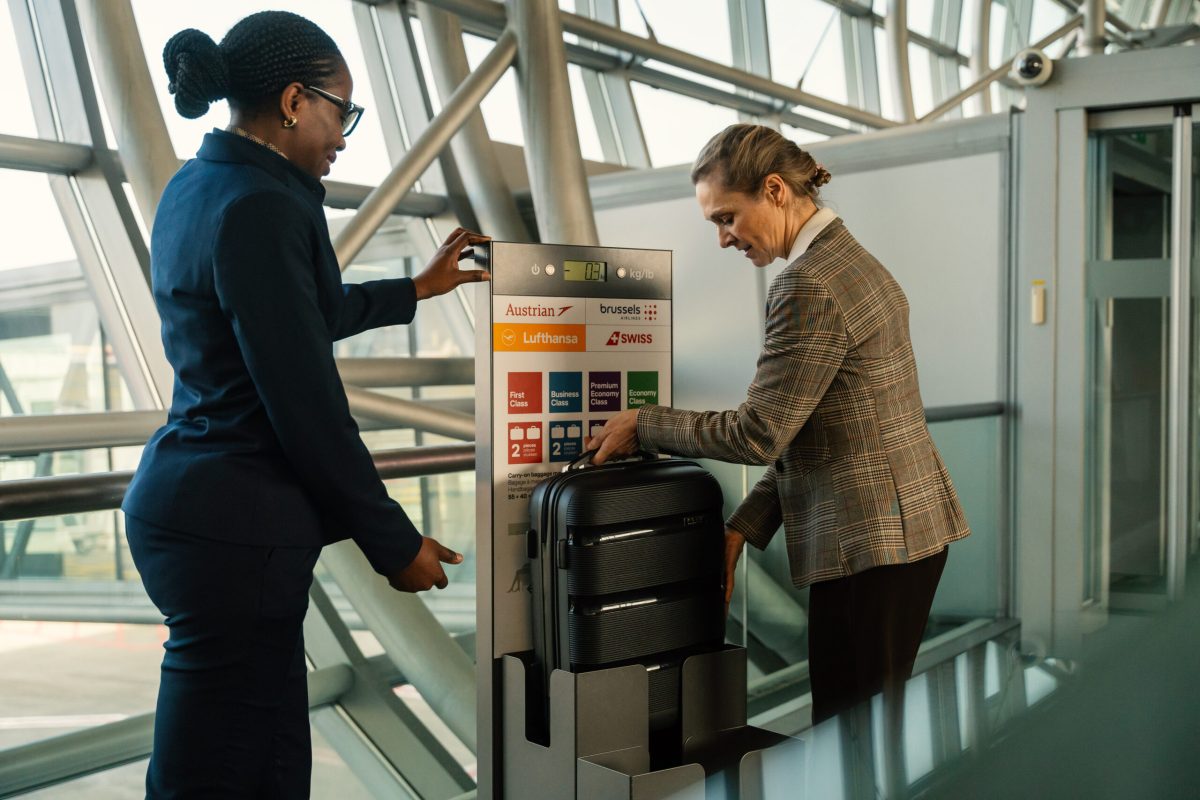 Two people examining a luggage size restriction frame at an airport