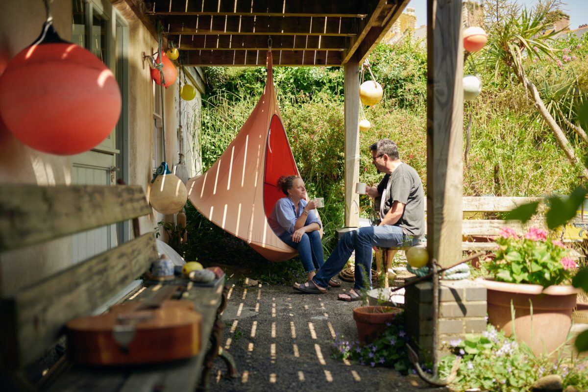 Two people sitting and talking in a covered garden patio area with hanging decorations