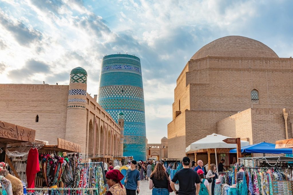 Kunya-Urgench's turquoise minaret rises above a bustling market scene.