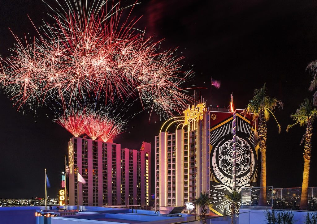 Fireworks explode above a Las Vegas casino with illuminated palm trees at night