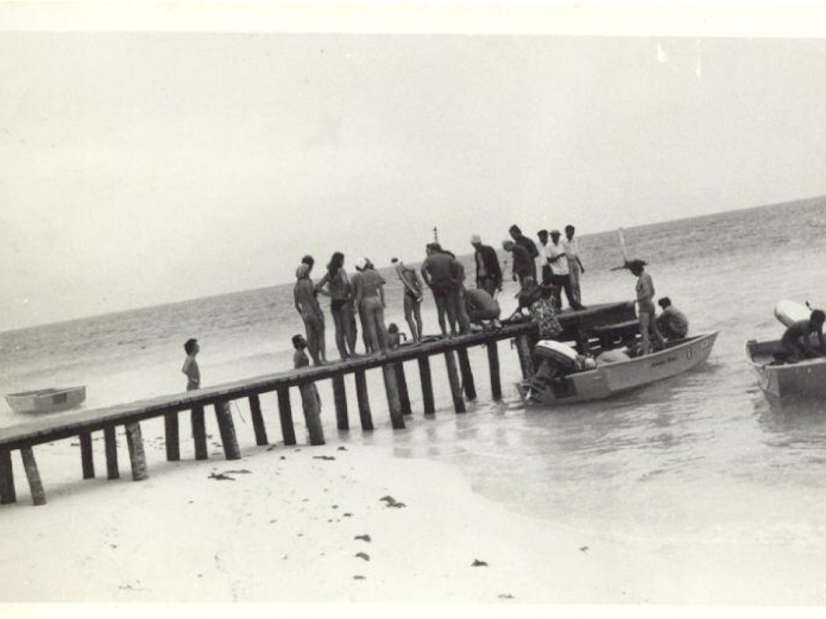 Vintage photograph of people boarding boats at a wooden pier on a Maldivian beach