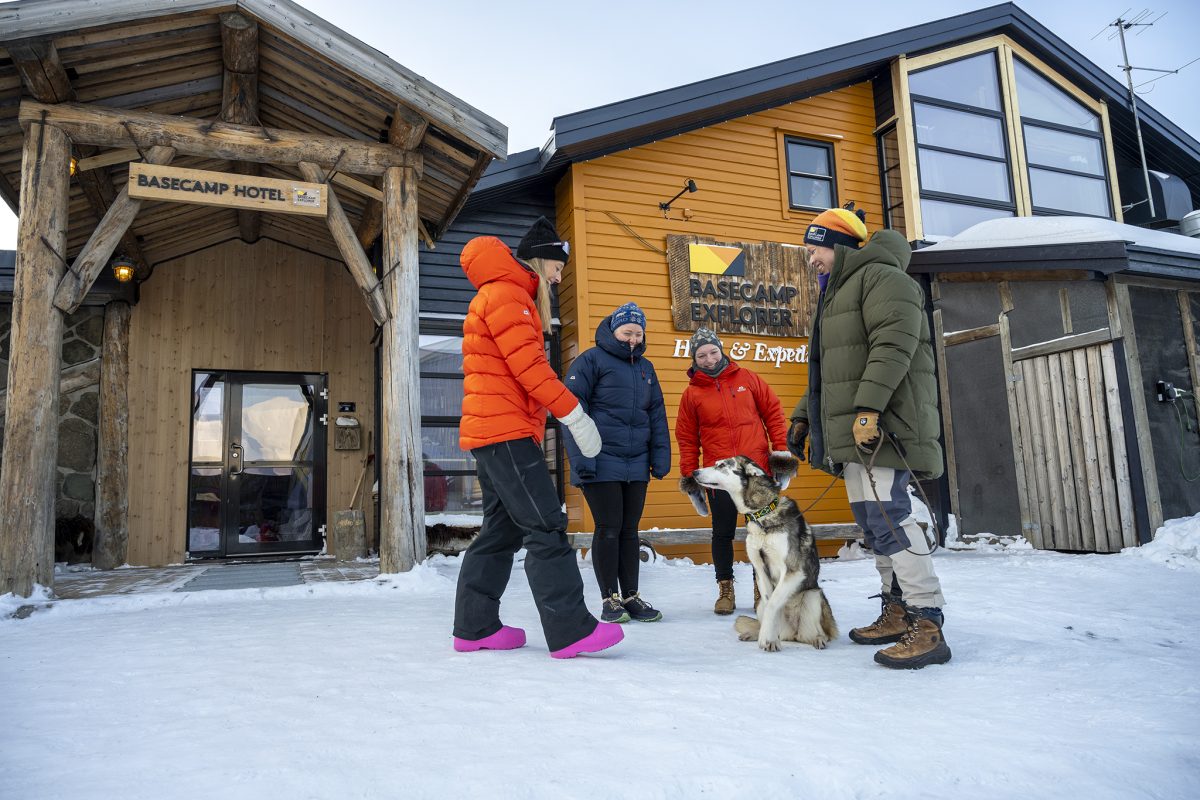 Visitors and a sled dog team outside a wooden cabin in snowy Svalbard landscape