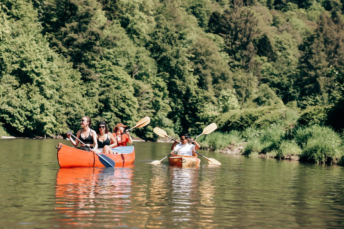 Visitors paddling orange kayaks on the Semois River surrounded by lush green forest