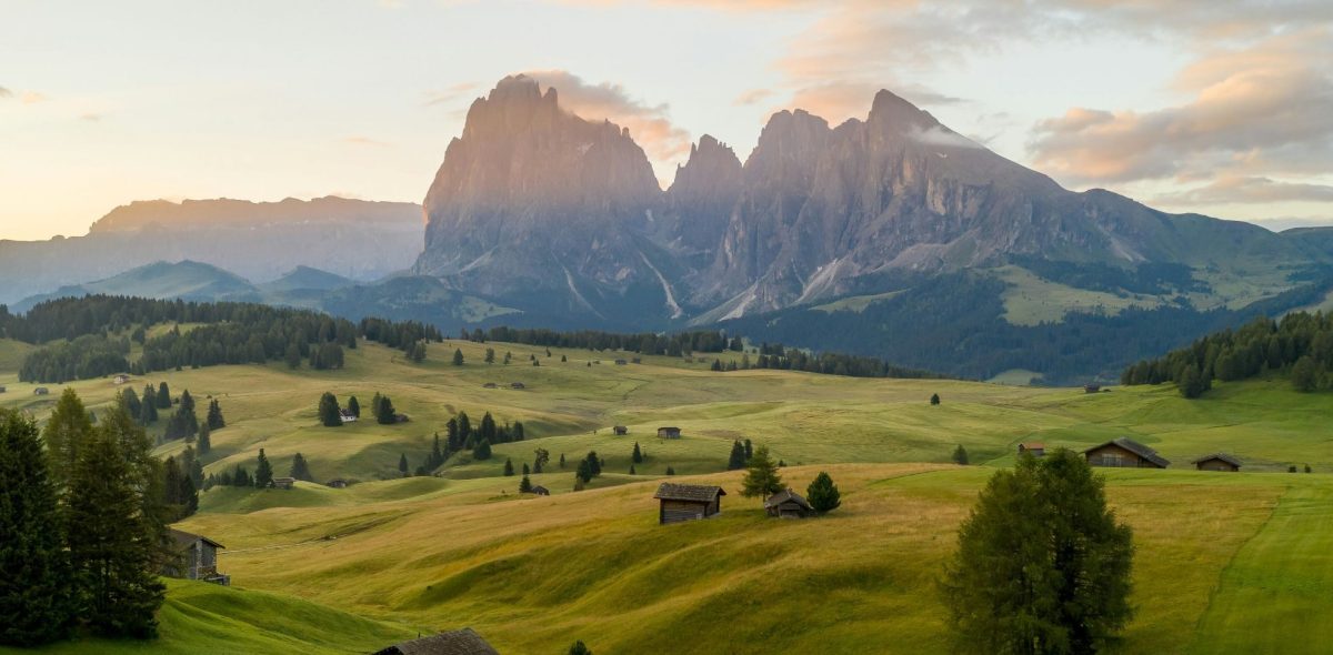 Alpine valley with dramatic mountain peaks and scattered farmhouses in green meadows