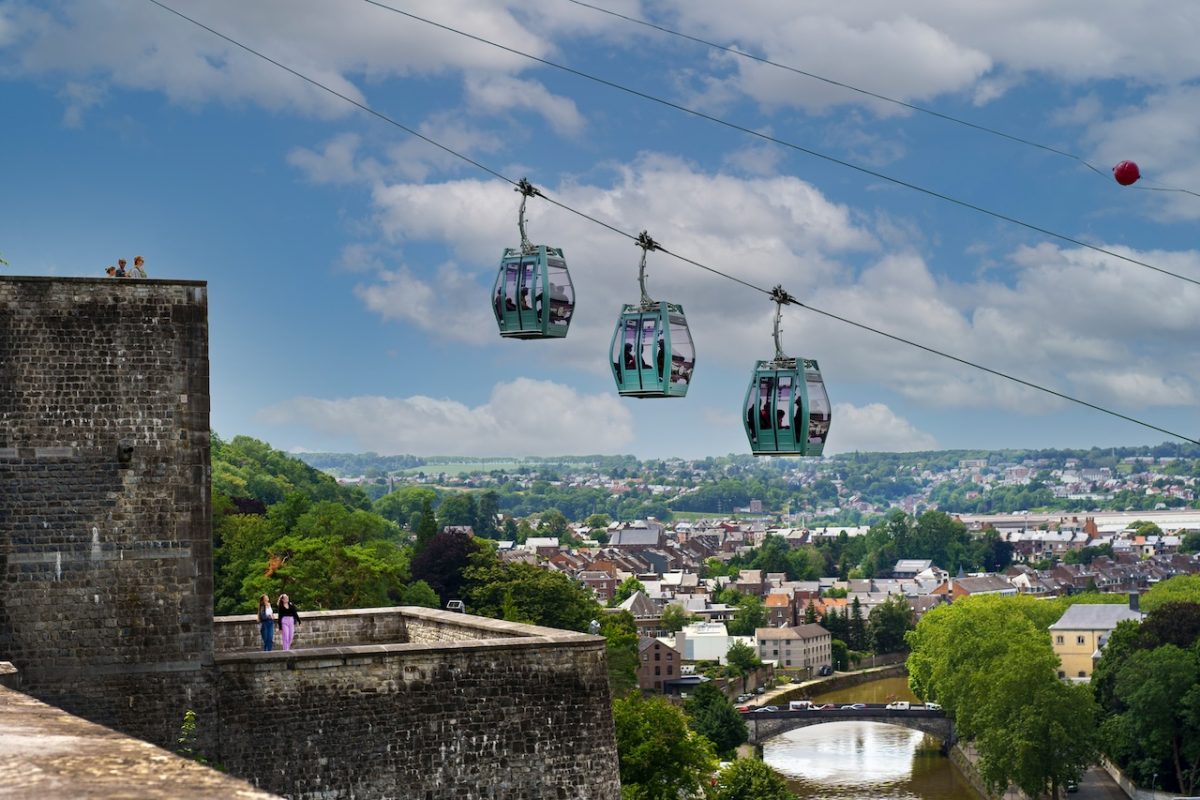 Cable cars descending from a medieval fortress overlooking a lush Walloon valley town
