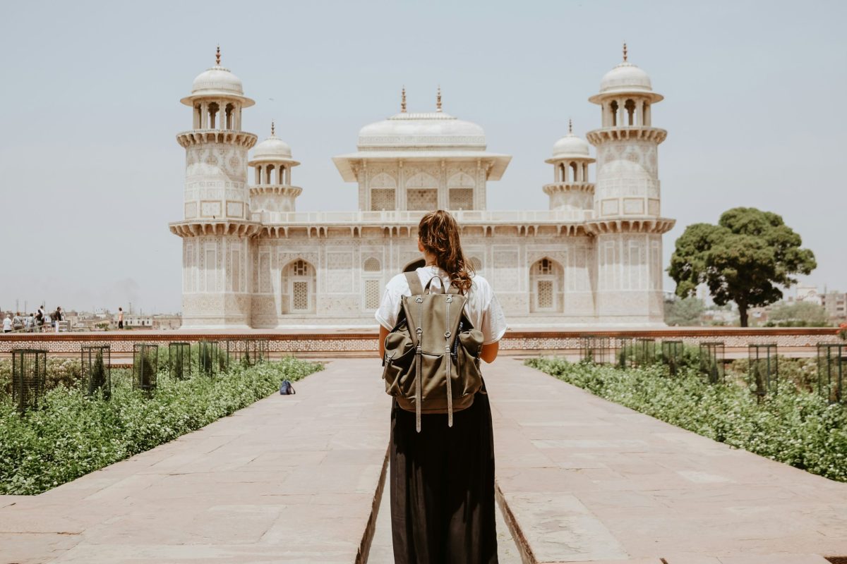Woman in traditional dress walking toward ornate white marble palace with symmetrical gardens