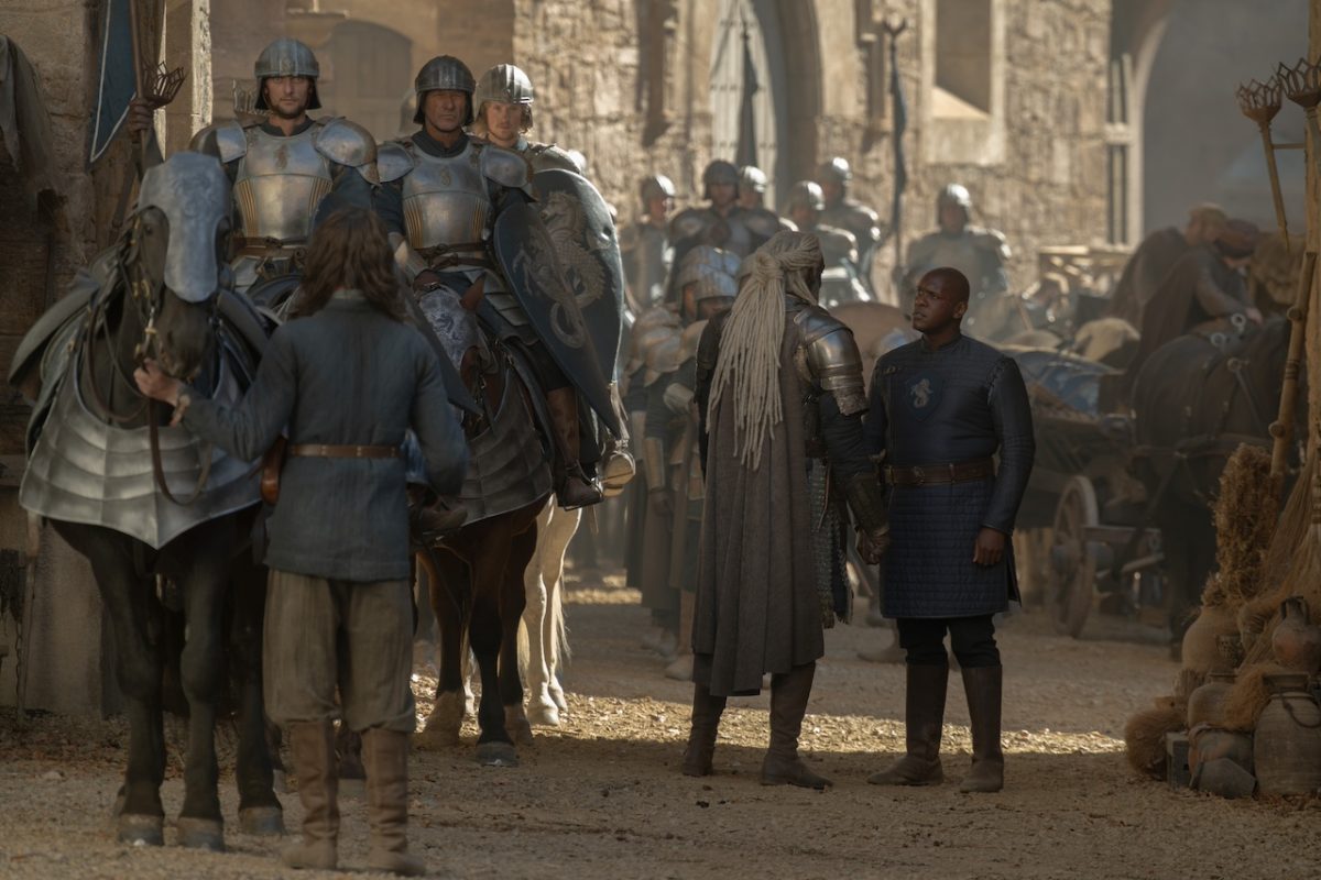 Medieval stone street scene with armored knights and crowd of extras in period costumes