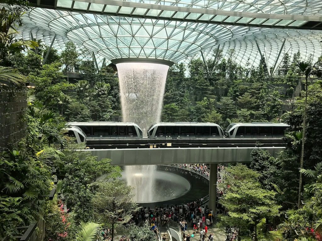 Modern airport terminal with train passing through lush indoor garden with glass ceiling