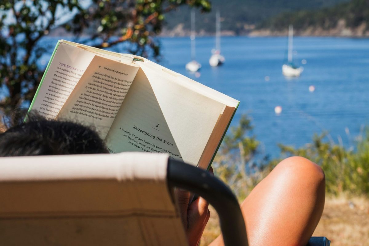 Open book held up against a coastal bay with sailboats in the distance