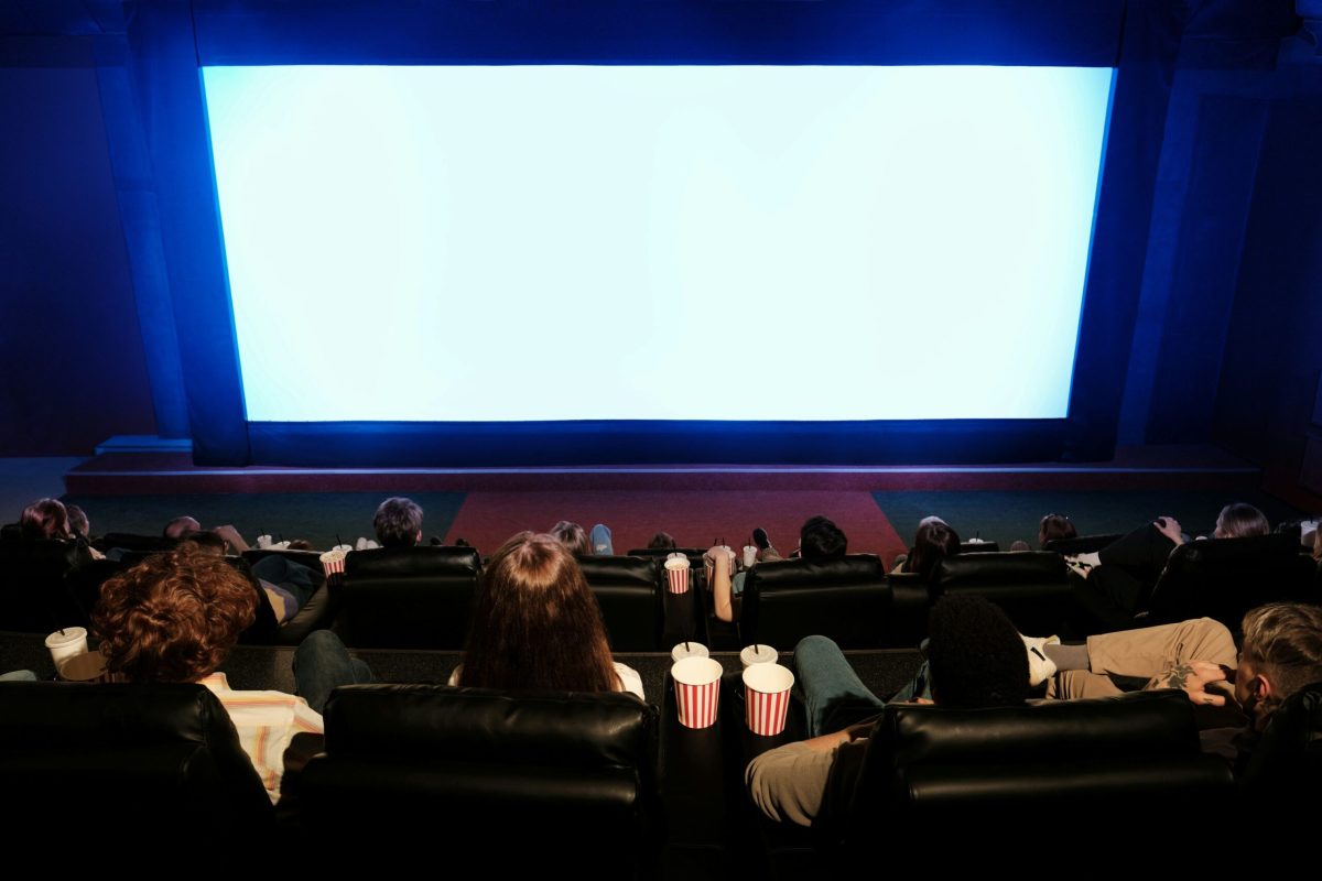 Movie theater audience seated in front of a large blank screen with popcorn visible