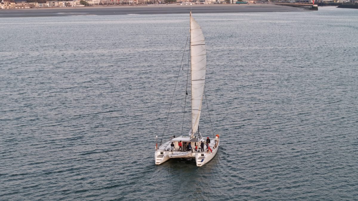 Wind-powered catamaran sailboat crossing the English Channel with white sail deployed