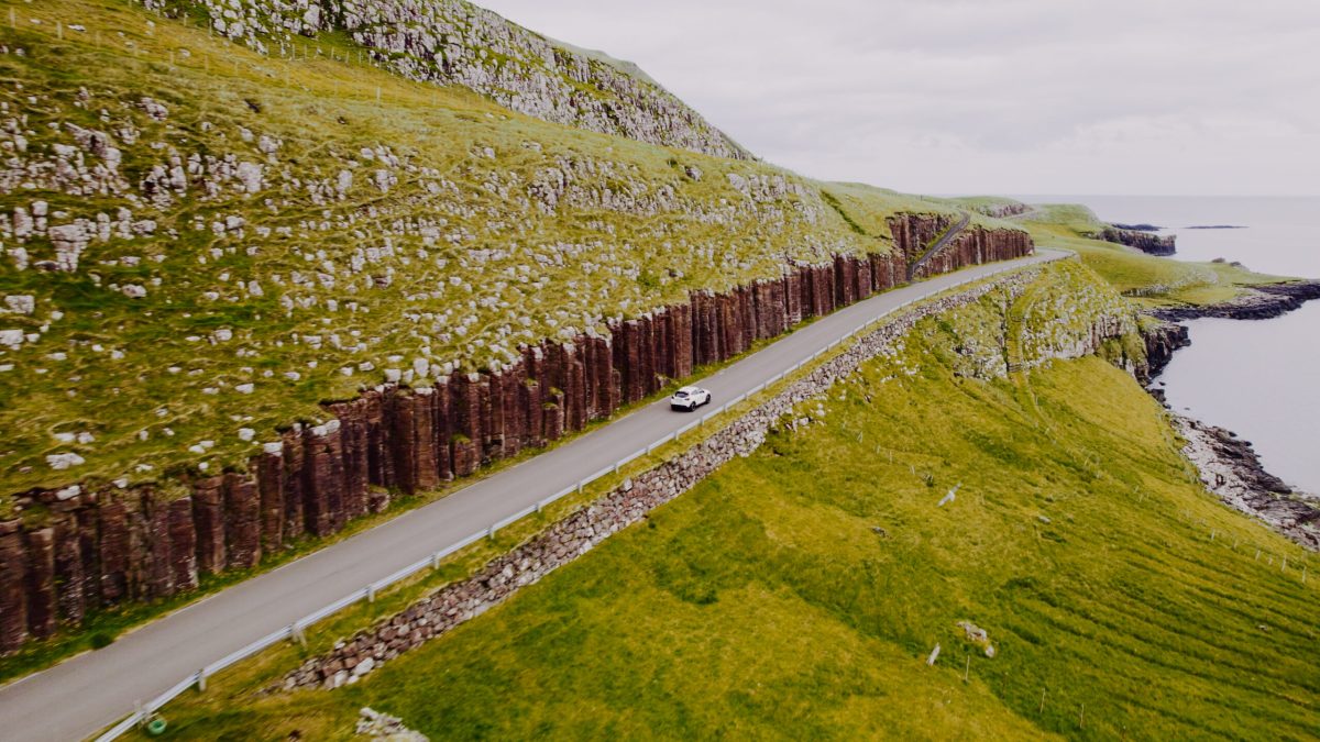 Winding road through moss-covered Faroe Islands landscape with wooden fence