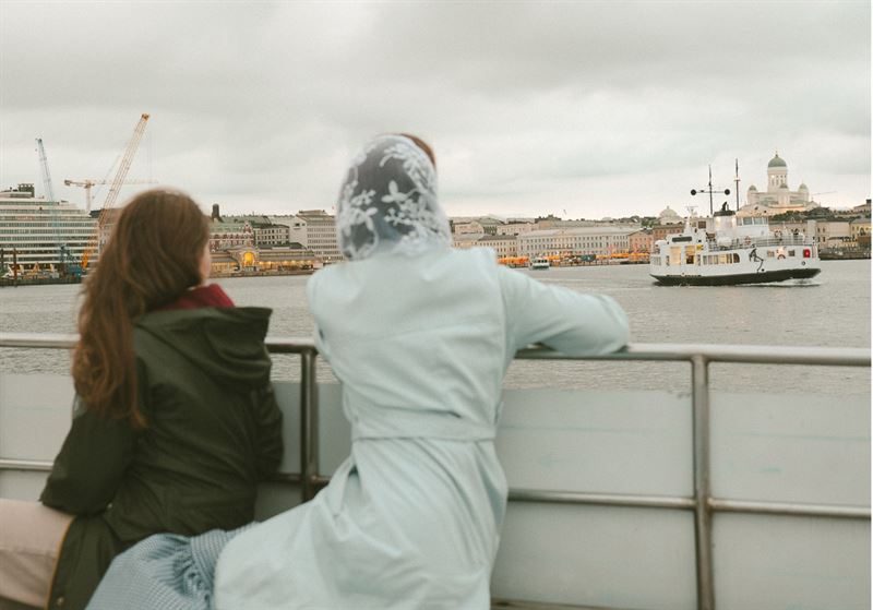 Woman and white-robed figure overlooking Helsinki waterfront from railing