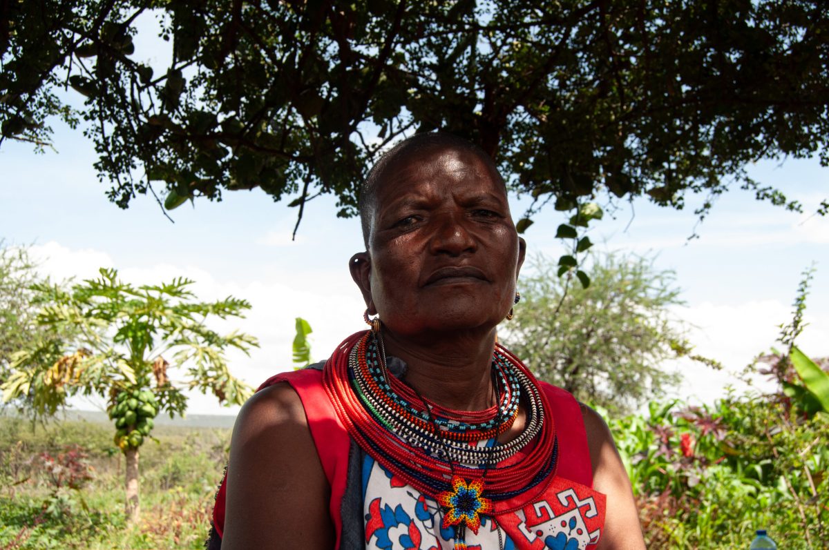 Woman in traditional Maasai attire stands beneath a tree in Naibunga Lower.