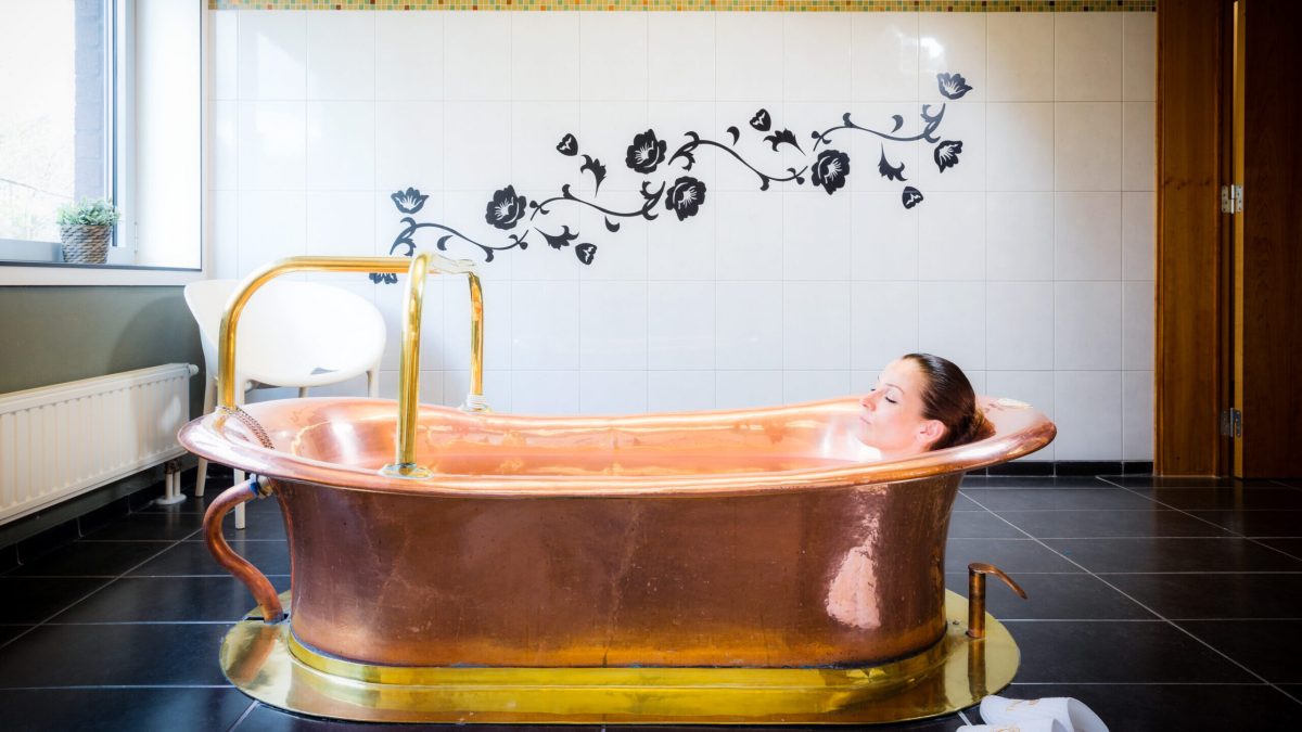 Woman relaxing in a luxurious copper bathtub filled with golden water